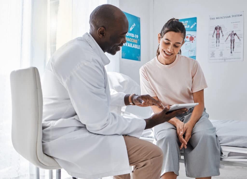 Doctor appointment or healthcare professional consulting a woman and explaining health using a tablet. A medical worker or GP talking to a patient and showing her scans or an online app in a hospital.