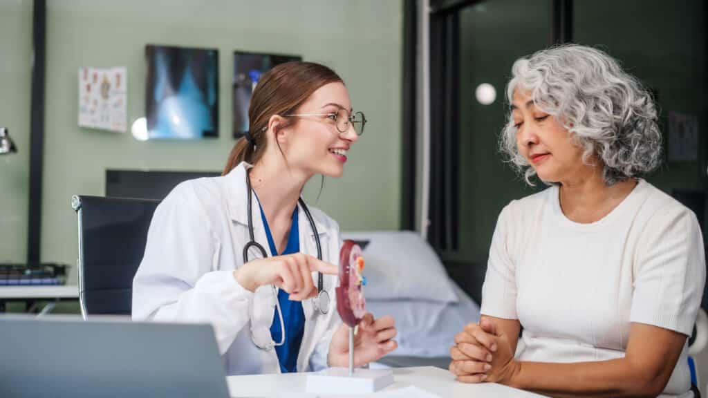 Caucasian woman sits at a desk, kidney model, gallstones, glomerulonephritis, acute and chronic kidney disease, infectious diseases, abnormal ureters, cysts, and urinary system cancer.