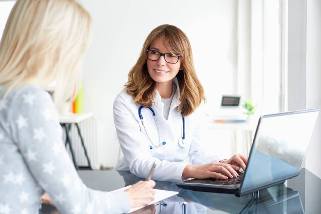 Shot of a middle aged smiling female doctor sitting in front of laptop and meeting with her patient.