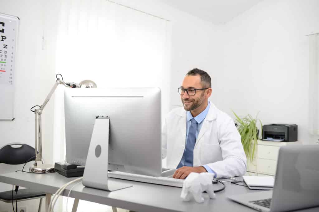 portrait of a handsome man male doctor in medical practice office working on computer