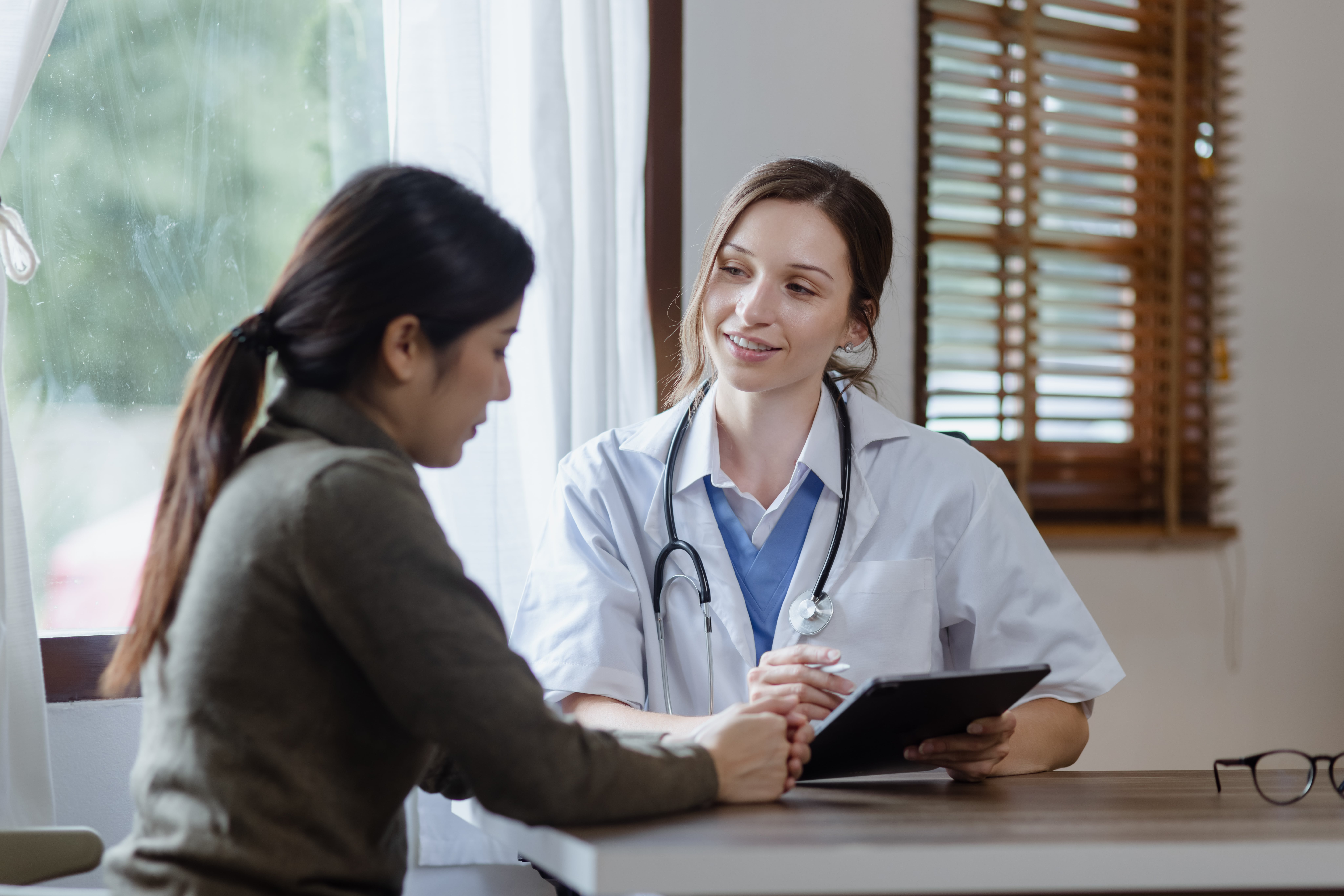 female doctor with female patient and telling advices sitting at workplace in clinic office, Healthcare and medical concept.