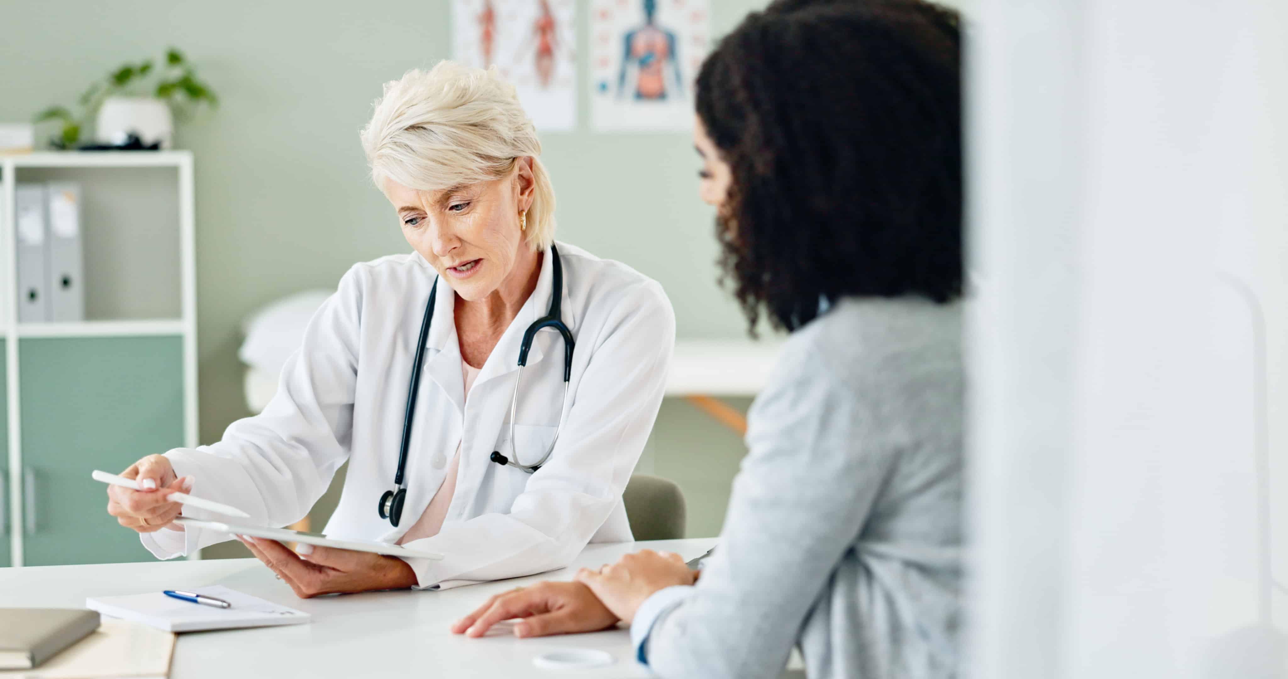 Mature woman, tablet and consulting with patient for medical results, diagnosis or prescription at hospital. Female person or cardiologist talking to client in consultation with technology at clinic.