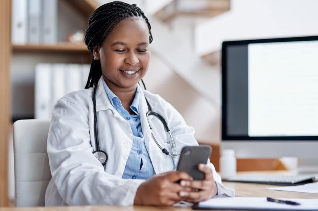 Shot of a young doctor using a cellphone while working in her office