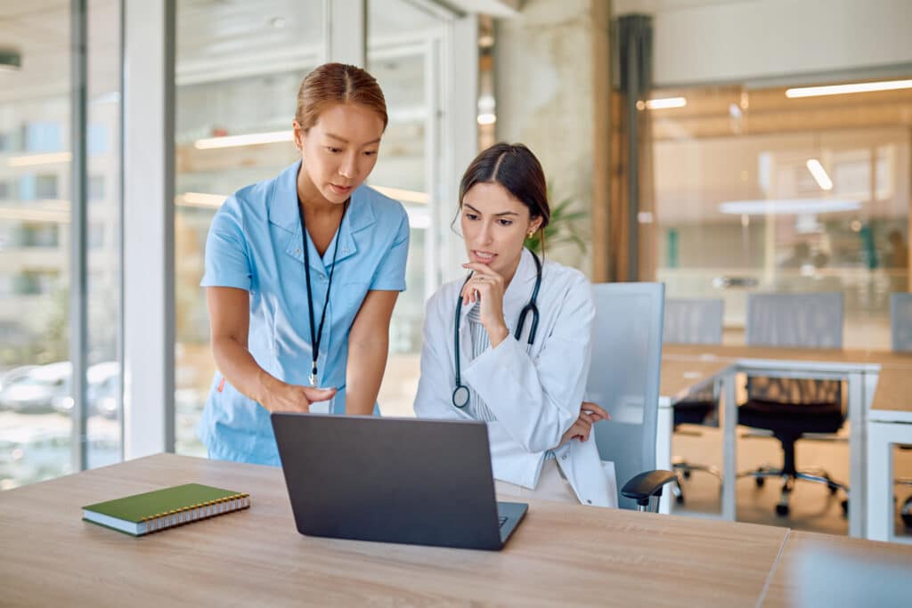 Doctors using laptop are discussing about a diagnosis in hospital meeting room